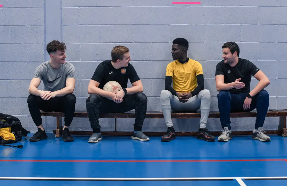A group of men talking on a bench in sports hall