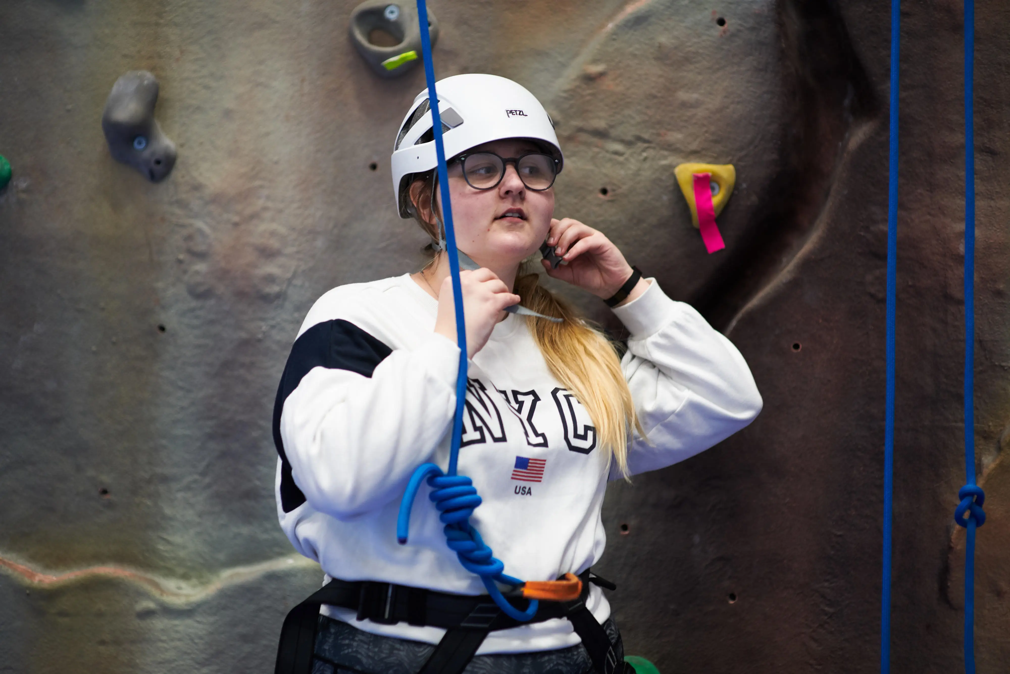 A participant clipping their helmet stood by climbing wall