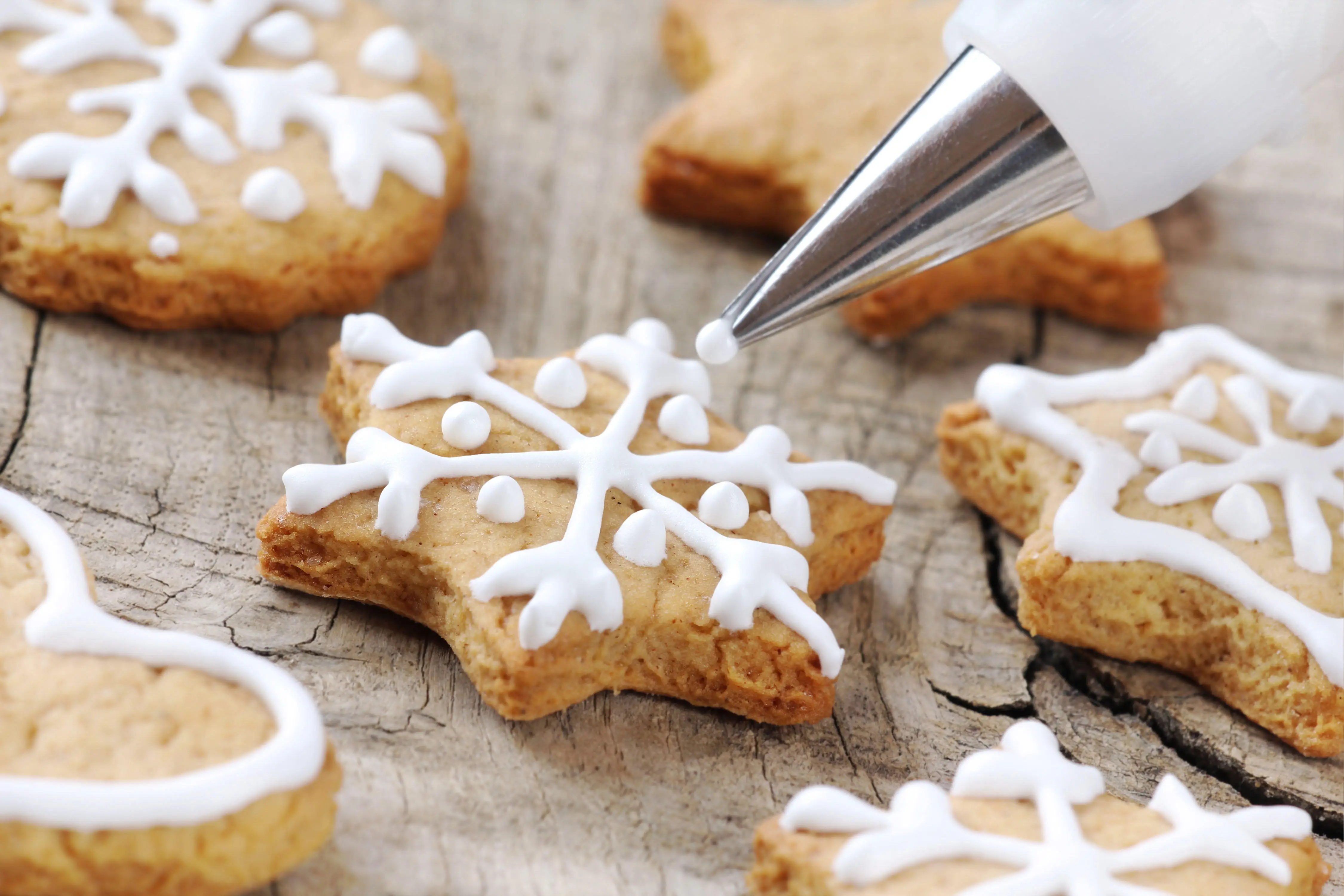 snowflake shaped biscuits being decorated with white icing