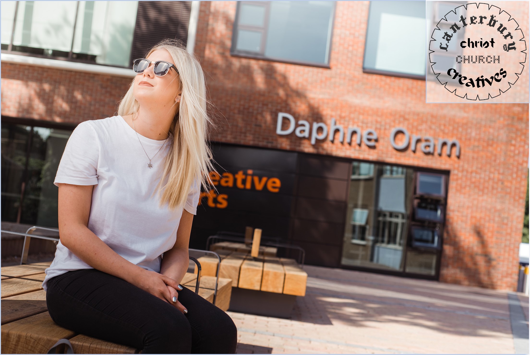 Student looking into the sky wearing her sunglasses, sitting outside the Daphne Oram building.