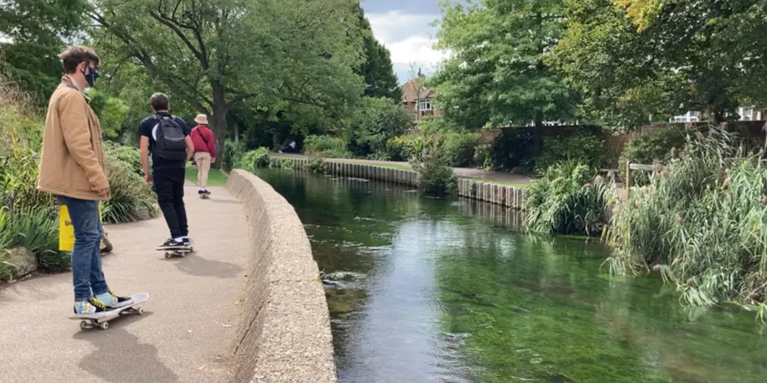 Photo of Canterbury river with 3 students skateboarding alongside on path