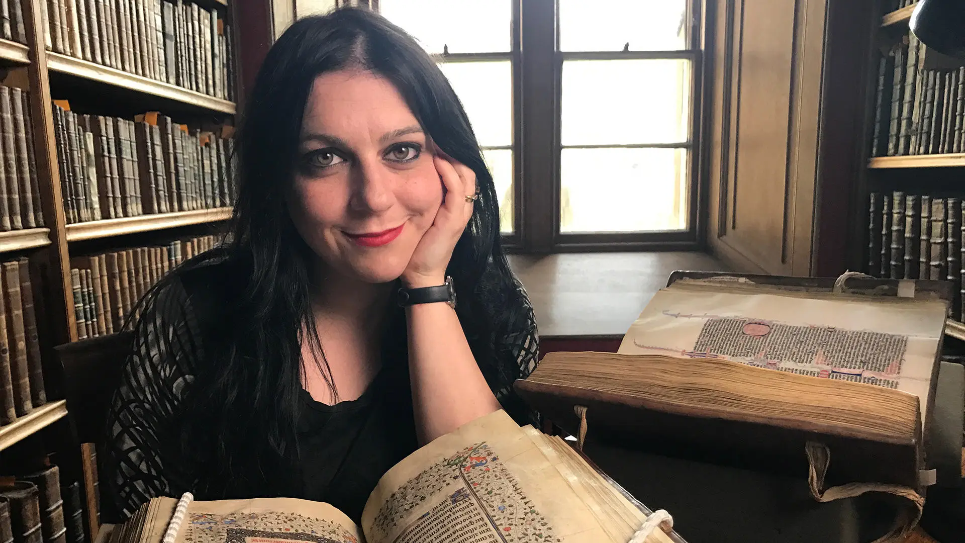 Dr Janina Ramirez in a library setting with an open medieval book