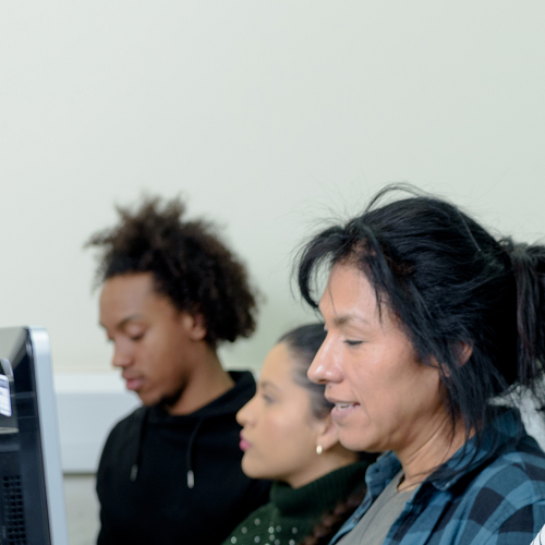 Four people are working at computers. A bearded man closest to the camera is smiling.