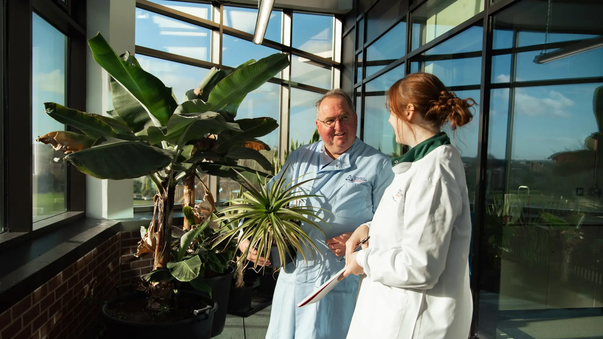 two people wearing lab coats looking at a plant