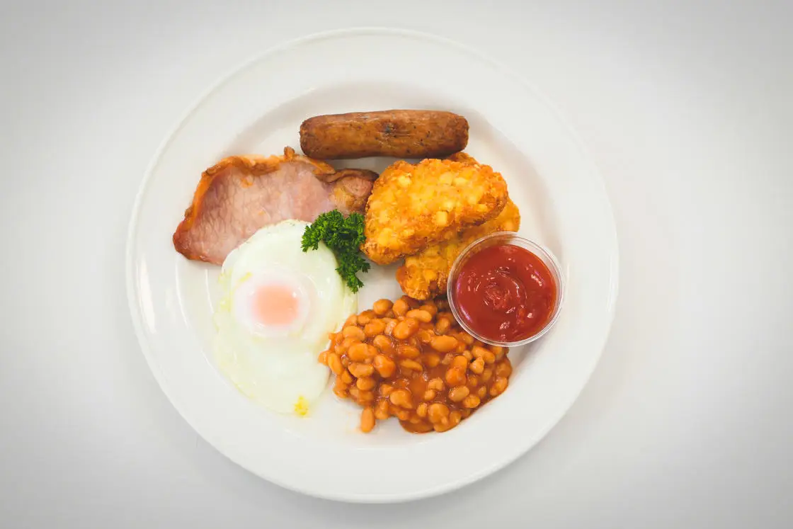 A plate of a cooked breakfast - bacon, sausage, hash browns, fried egg, beans and ketchup.